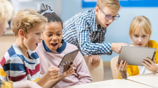 Niños y niñas sorprendidos mirando tablets en clase.